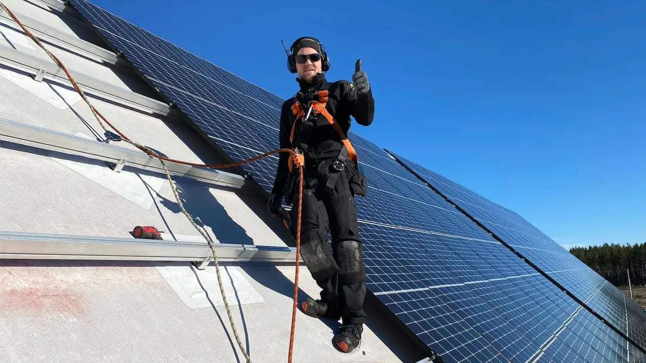 Installat&ouml;r ger tummen upp vid solcellsmontering. Arbetet sker i tre faser p&aring; taket med solpaneler och s&auml;kerhetsutrustning.