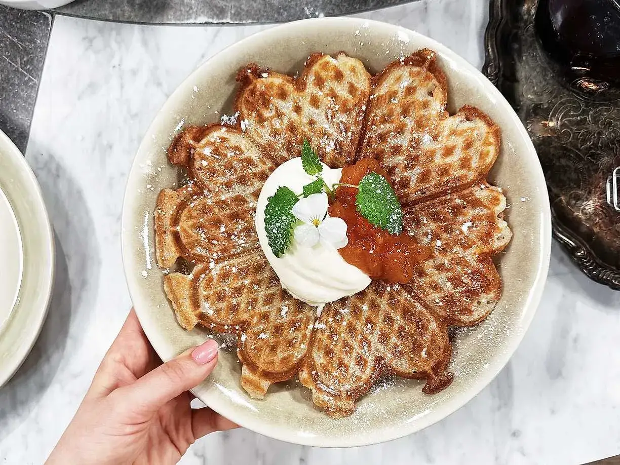 En vacker tallrik med glutenfria våfflor formade som en blomma, toppad med grädde, sylt och mynta.