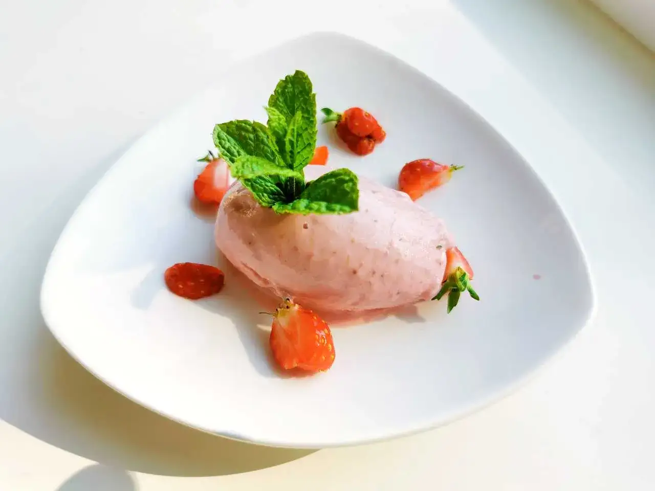 En portion krämig jordgubbsglass, gjord med en frozen yoghurt glassmaskin, garnerad med färska jordgubbar och mynta.