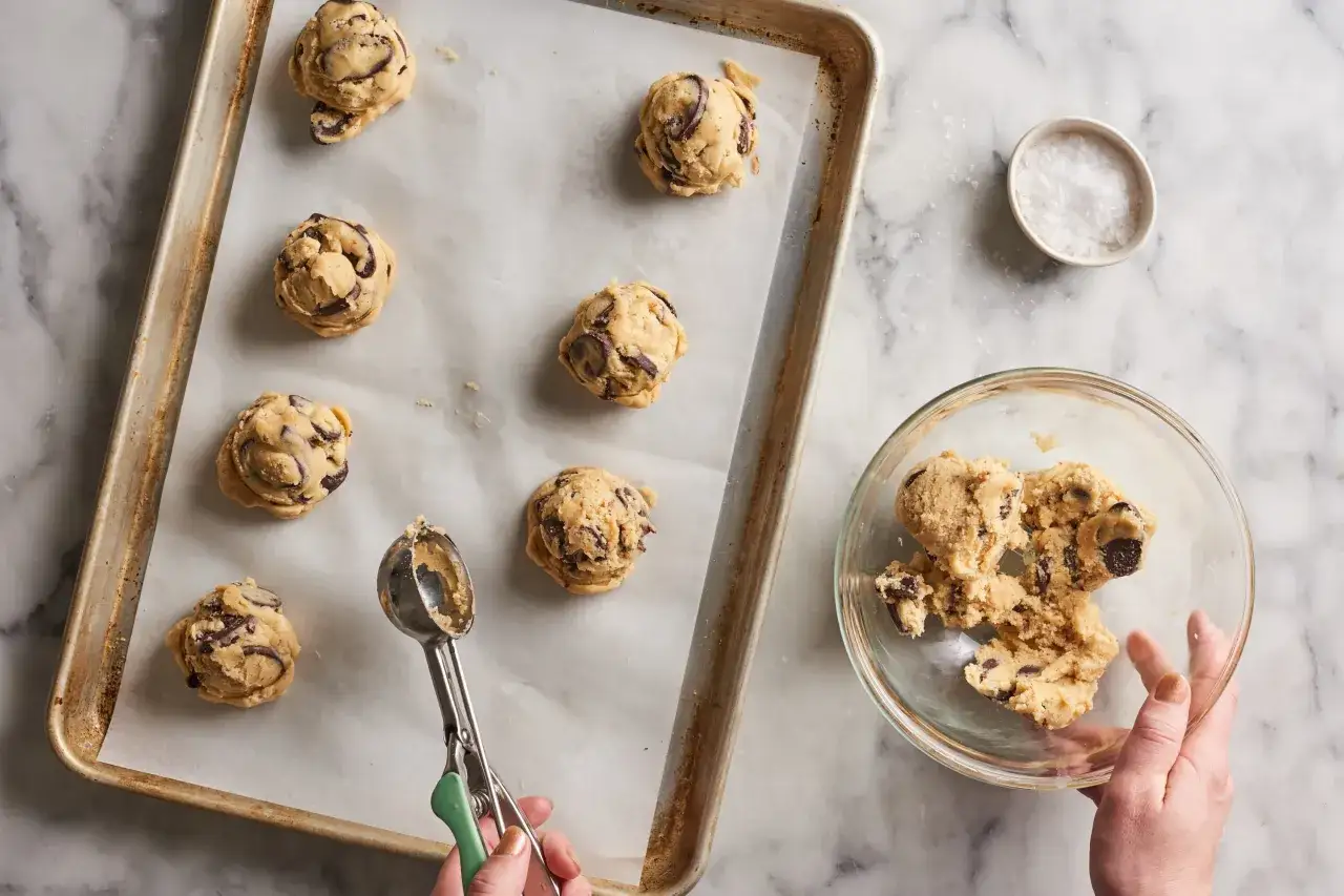Des boules de pâte à cookie, riches en pépites de chocolat, attendent sur une plaque de cuisson. La texture de la pâte à cookie est visible, prête à être transformée en délices.