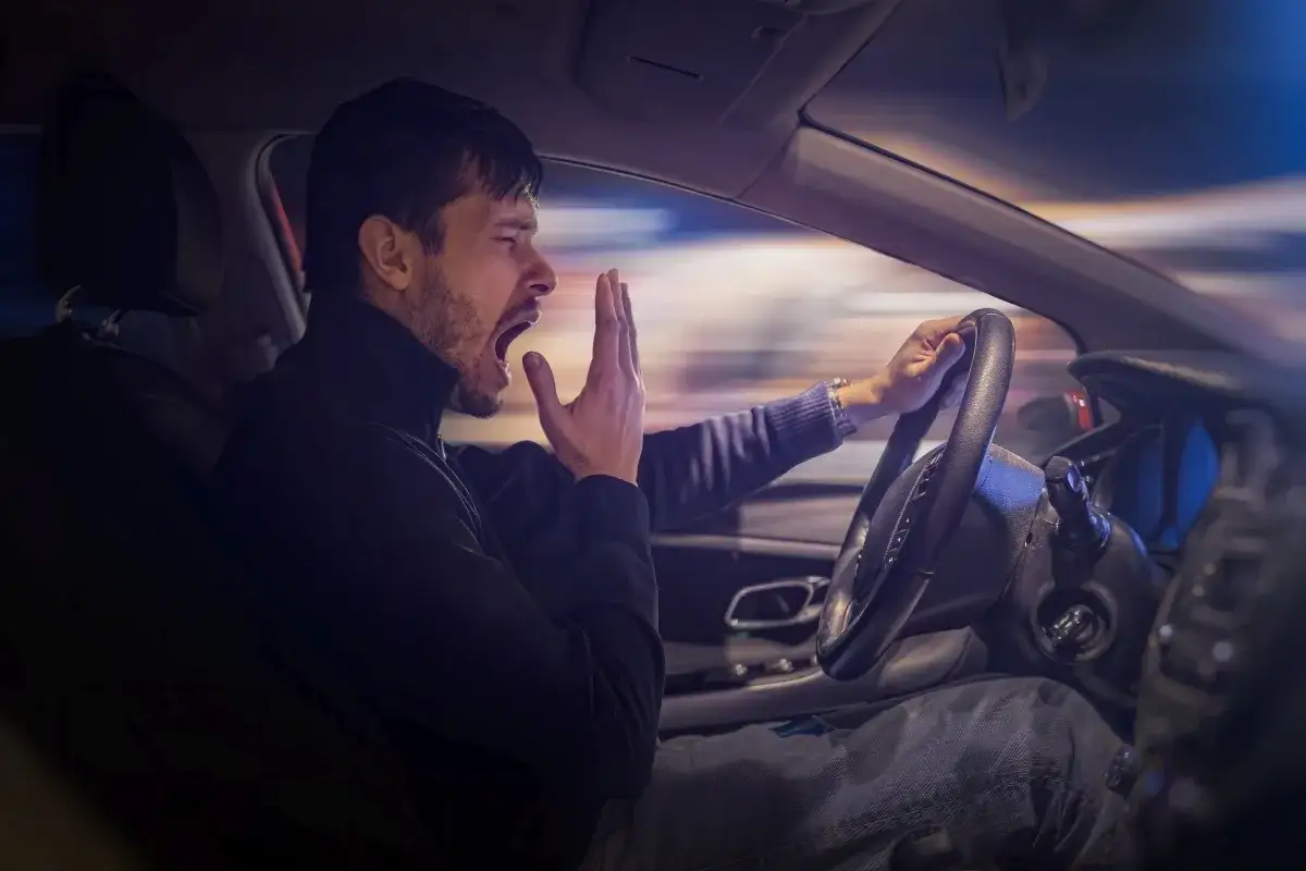 Mężczyzna ziewając za kierownicą, walczy ze snem. Pamiętaj, jak nie zasnąć za kierownicą – zrób przerwę!