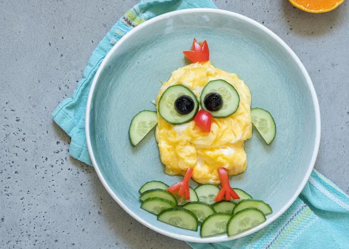 Un pollito de huevo revuelto con ojos de pepino y aceituna, ideal para cenas para ni&ntilde;os de 2 a 3 a&ntilde;os.
