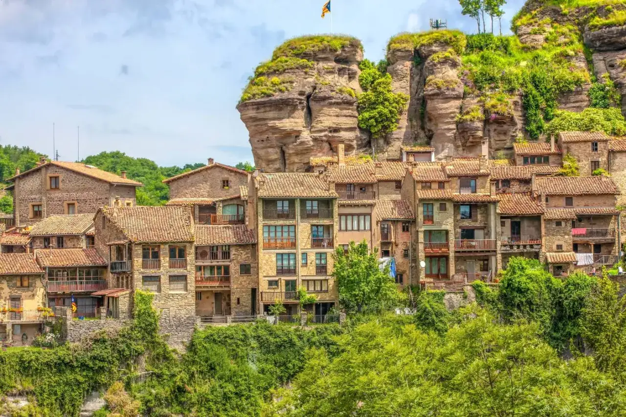 Pueblo de piedra con tejados rojos, anidado bajo un acantilado. Las **rutes per Osona** te llevan a este lugar con encanto.