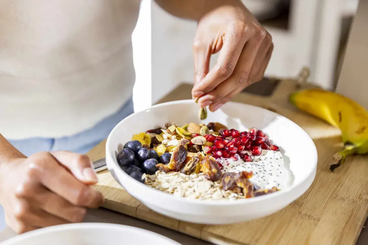 Eine Sch&uuml;ssel M&uuml;sli mit Beeren, N&uuml;ssen und Granatapfelkernen wird garniert. Die gesunden Polyphenole wirken sich positiv auf die Gesundheit aus.