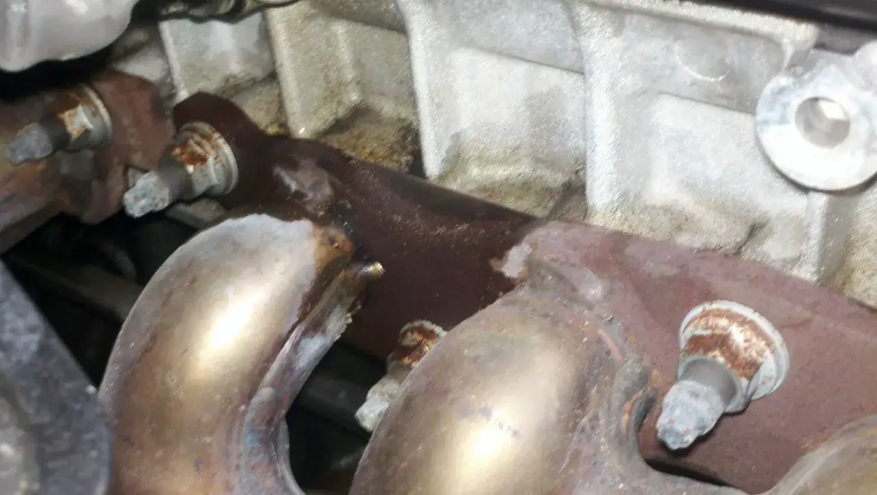 Rdzawe śruby i metalowe elementy silnika, z kt&oacute;rych wydobywa się dym spod maski i czuć zapach spalenizny.