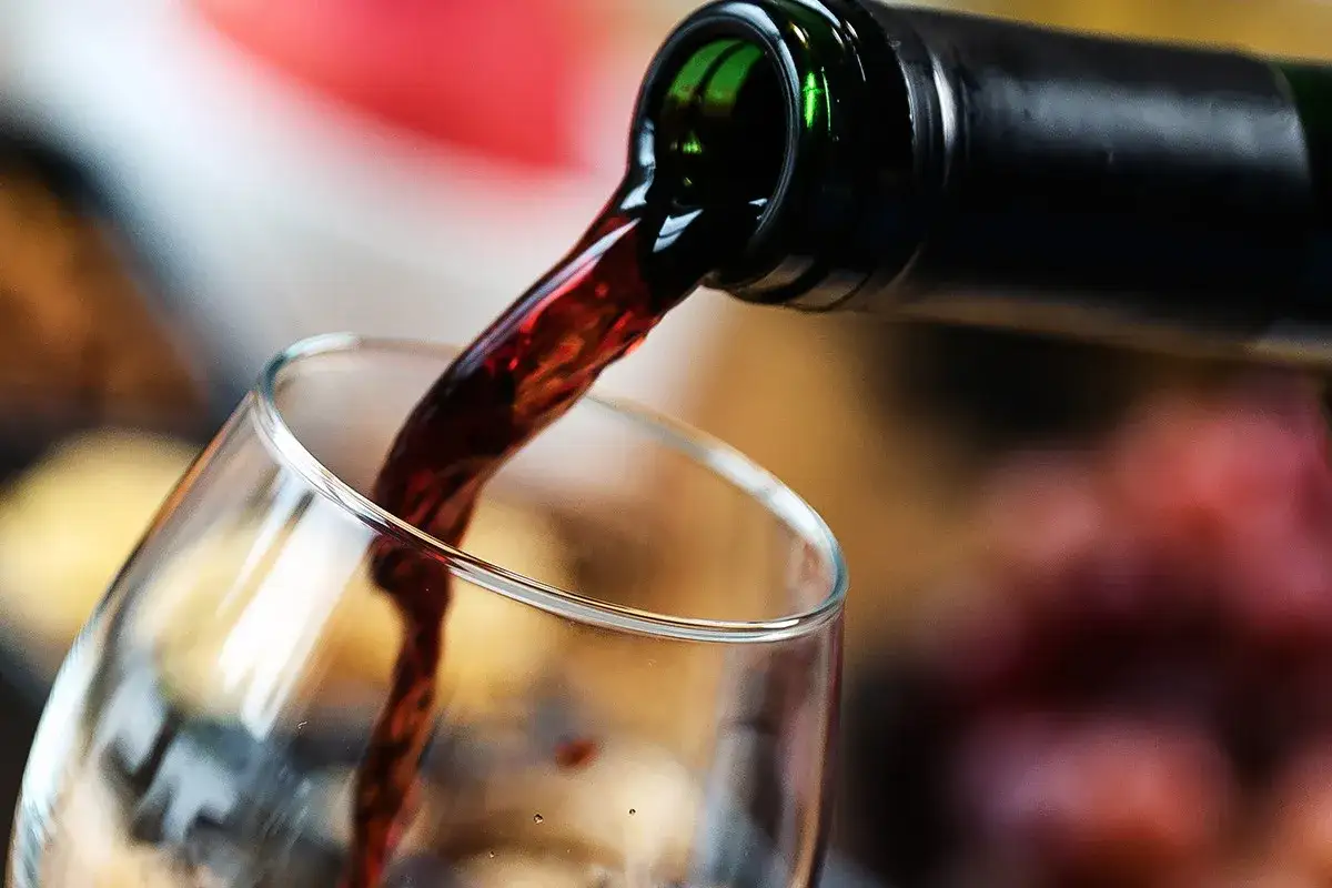 Ciemnoczerwone, mętne wino leje się z butelki do kieliszka.