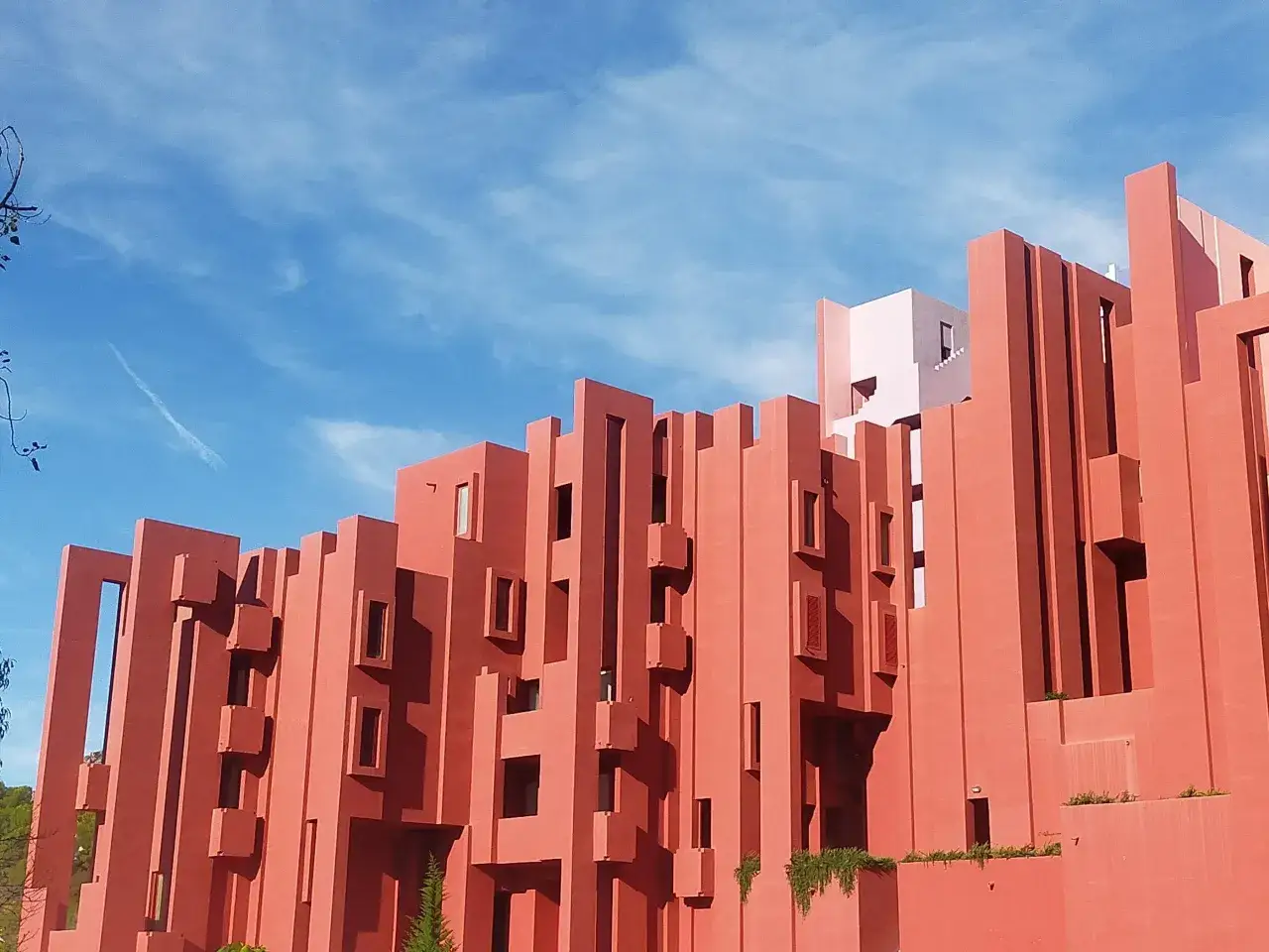 Edificio de arquitectura brutalista en Calpe, con su característica muralla roja y un cielo azul con nubes.