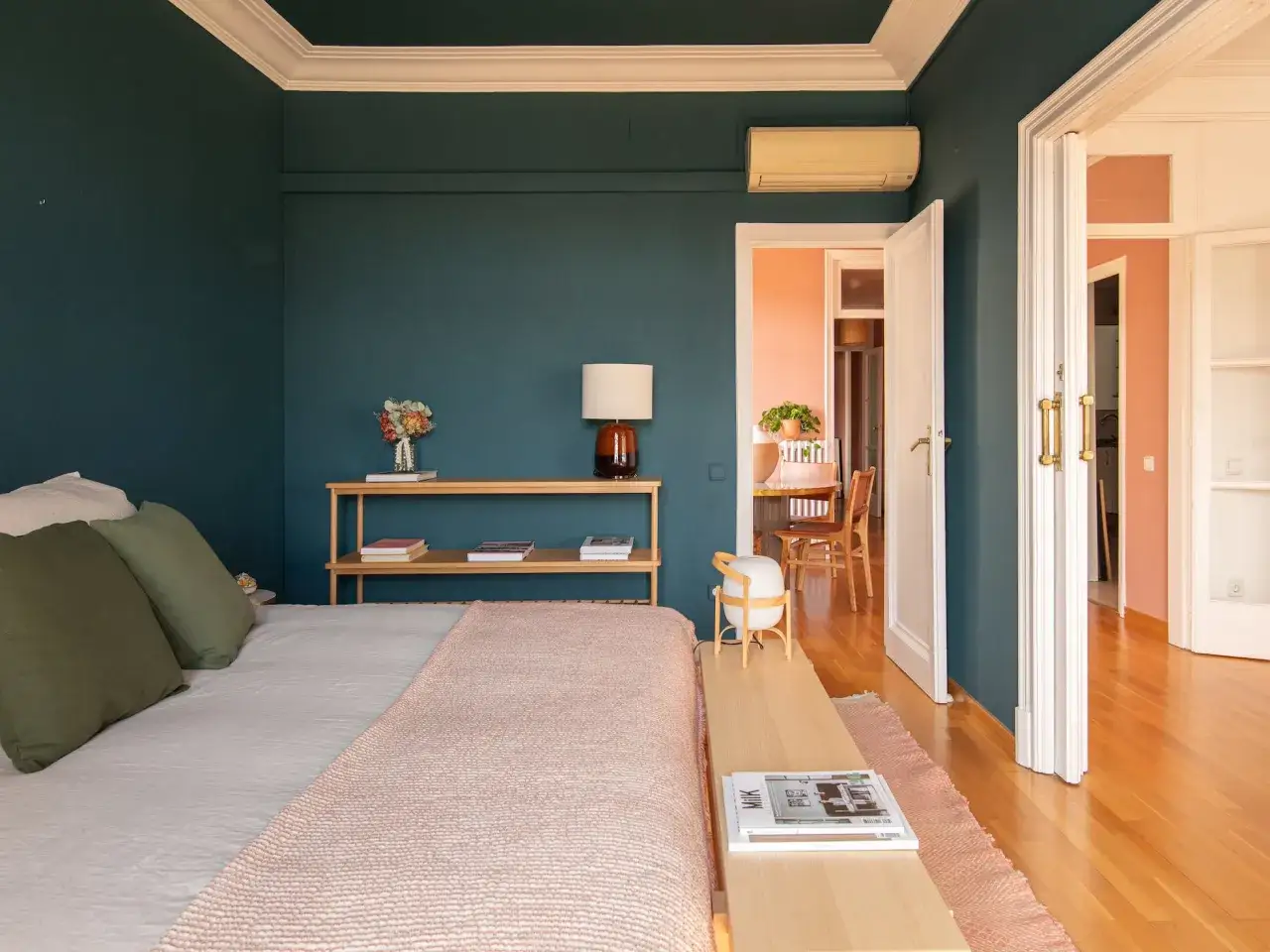 Habitaci&oacute;n con paredes azul oscuro y techo blanco. La cama tiene mantas rosas y verdes. Se ve un comedor al fondo. &iquest;Qu&eacute; se pinta primero el techo o las paredes?