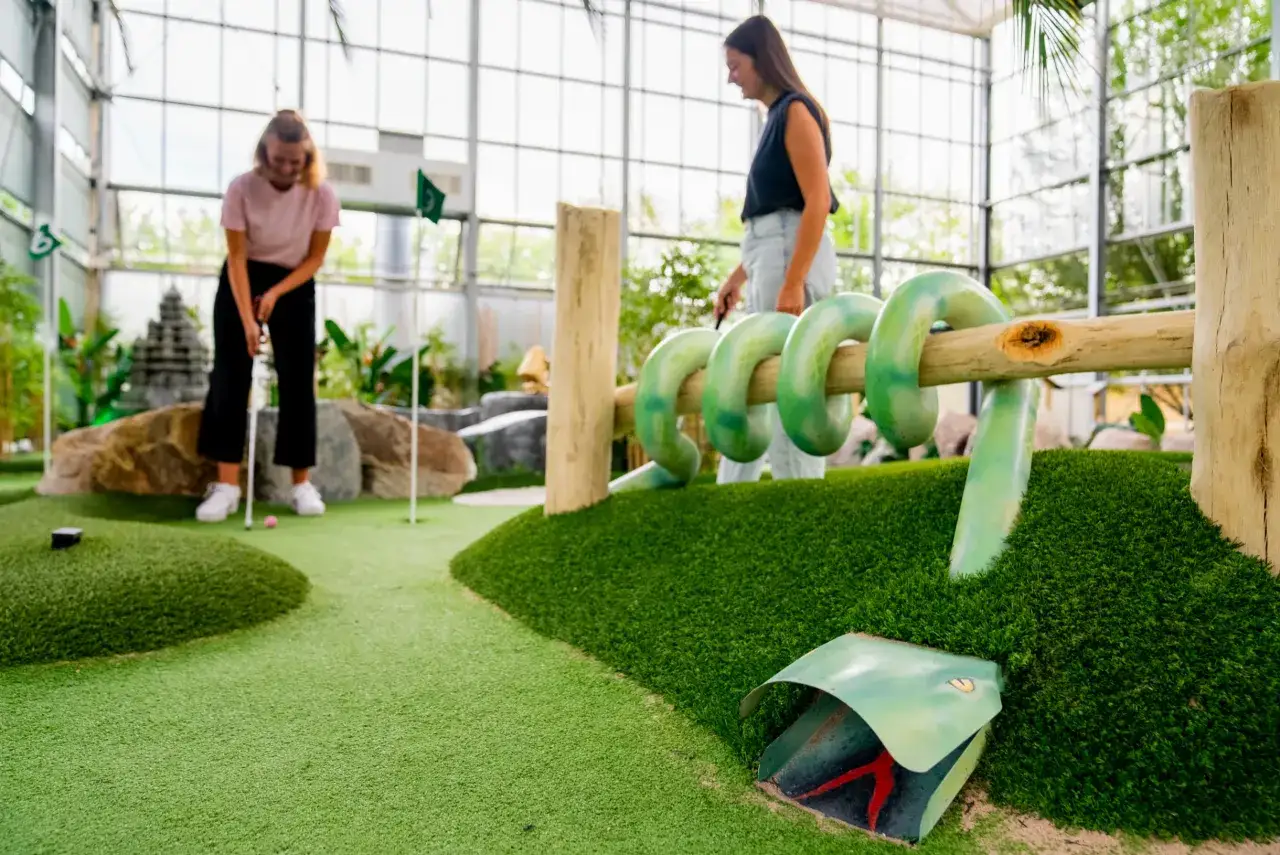 Zwei Frauen spielen Minigolf Gummersbach. Eine schl&auml;gt ab, die andere beobachtet die Bahn mit Schlangen-Hindernis.