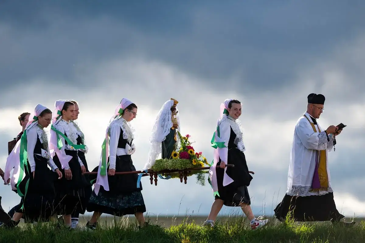Procesja z figurą Matki Boskiej, niesioną przez kobiety w tradycyjnych strojach. Ksiądz idzie z tyłu, czytając z książki. Może to być związane z tradycją, gdzie podatek na kościół jest dobrowolny.