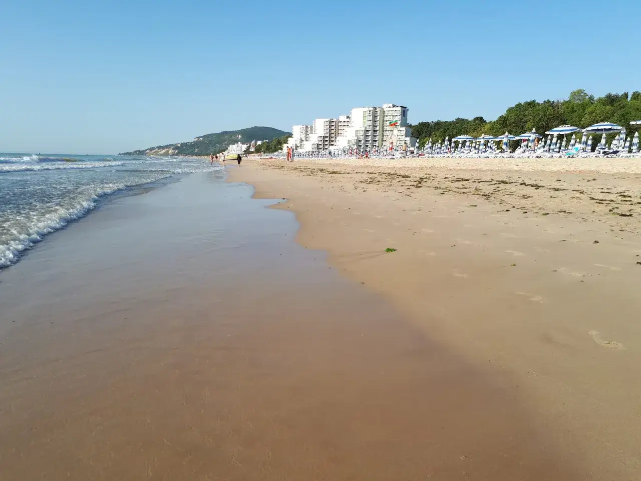 Piękna plaża w Albena Bułgaria. Fale obmywają piaszczysty brzeg, a w oddali widać hotele i rzędy parasoli.