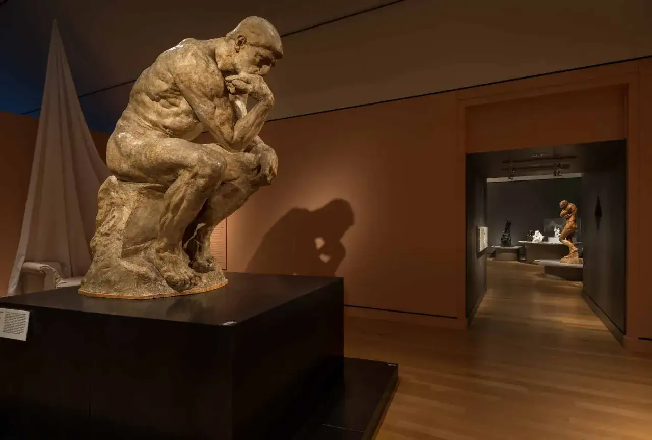 Auguste Rodin Myśliciel, siedzący w pozie kontemplacji, rzuca głęboki cień na ścianę muzeum.