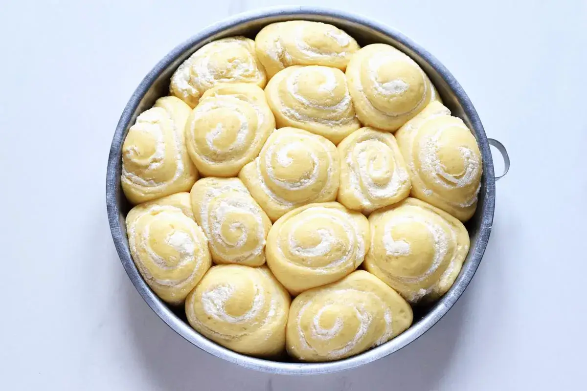 Torta di rose lievitata, pronta per essere infornata, con soffici spirali di pasta spolverate di zucchero a velo.
