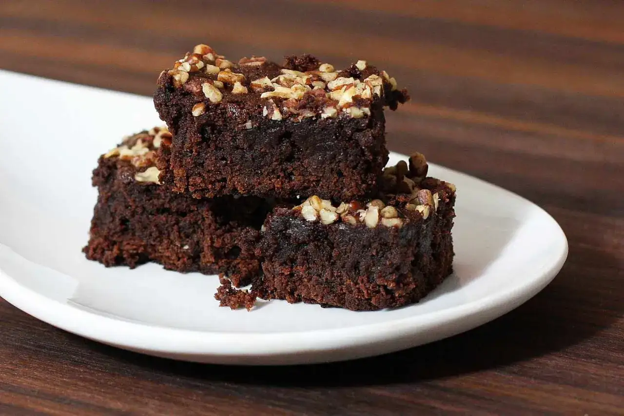 Pyszne brownie Ani gotuje, posypane orzechami, na białym talerzu.