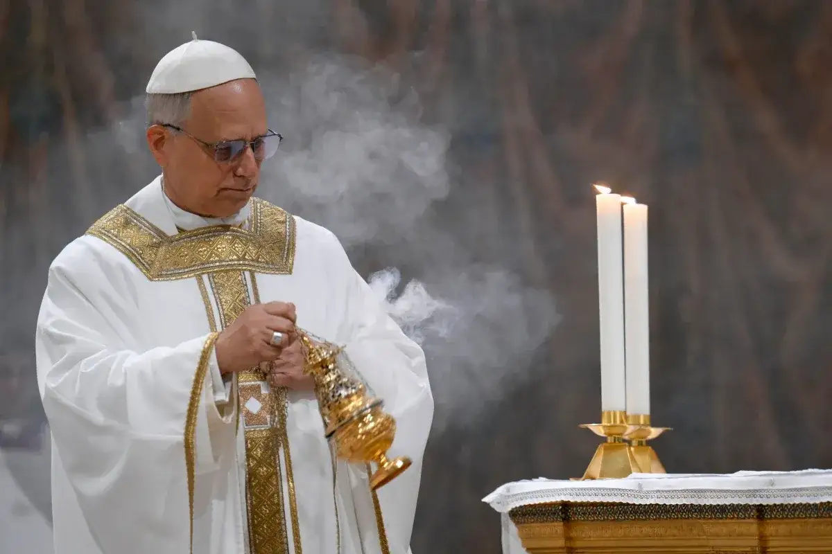 Biskup w białej szacie z haftem, trzymający kadzielnicę, podczas uroczystości symbolizującej jego pontyfikat.
