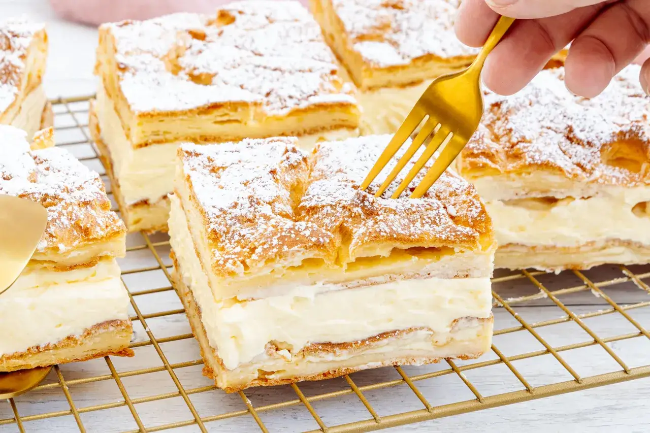 Ein goldener Löffel sticht in ein Stück polnischer Puddingkuchen, bestäubt mit Puderzucker.