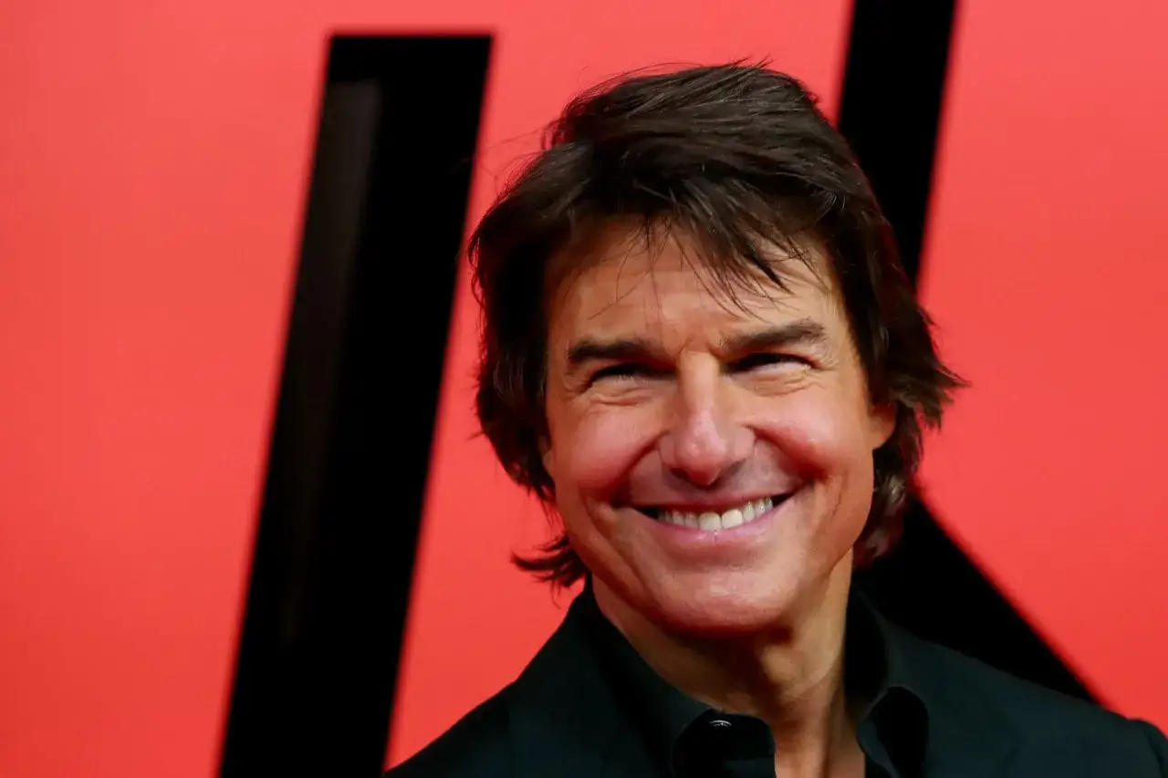 Uśmiechnięty Tom Cruise na czerwonym tle. Zastanawiasz się, ile zarabia Tom Cruise? Jego zarobki są imponujące!