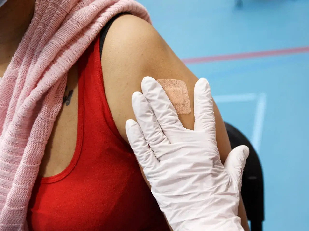 En hand i vitt handskar sätter ett plåster på armen efter att ha fått vaccin för att fylla på grundskydd.