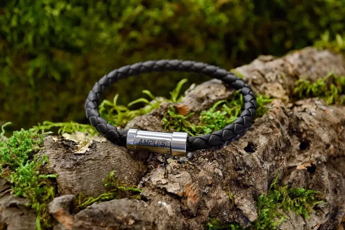 Schwarzes, geflochtenes Lederarmband mit silbernem Verschluss, das auf moosbewachsenem Holz liegt. Perfekt f&uuml;r die Pflege und das lederarmband reinigen.