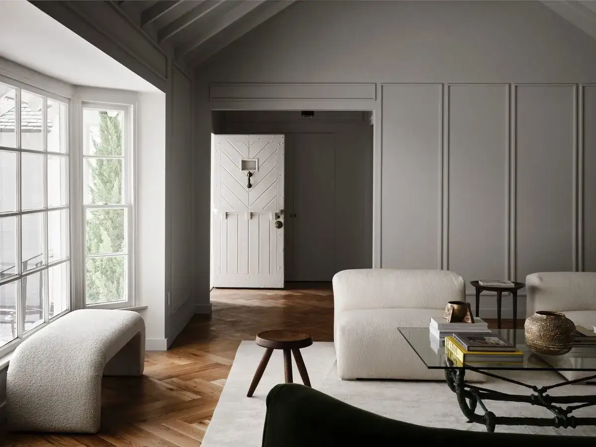 Ein Wohnzimmer mit einem Hauch von **color drenching** durch die wei&szlig;en M&ouml;bel und die holzget&auml;felten W&auml;nde. Ein einzigartiges wei&szlig;es Scheunentor f&uuml;hrt in einen Flur.