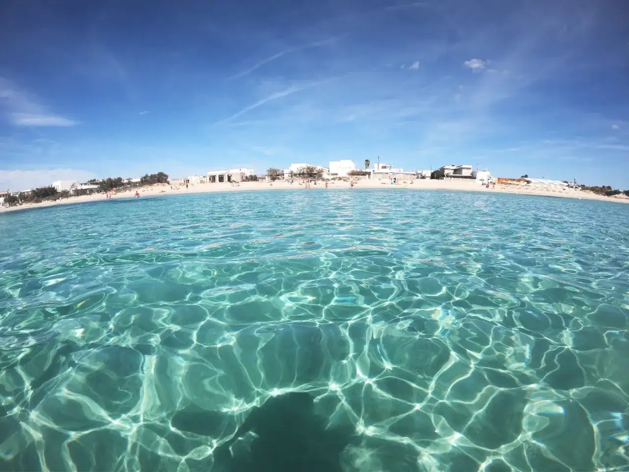 Crystal clear water laps a sandy beach lined with white buildings. This is the perfect spot to ask: where to stay in Puglia for beaches?