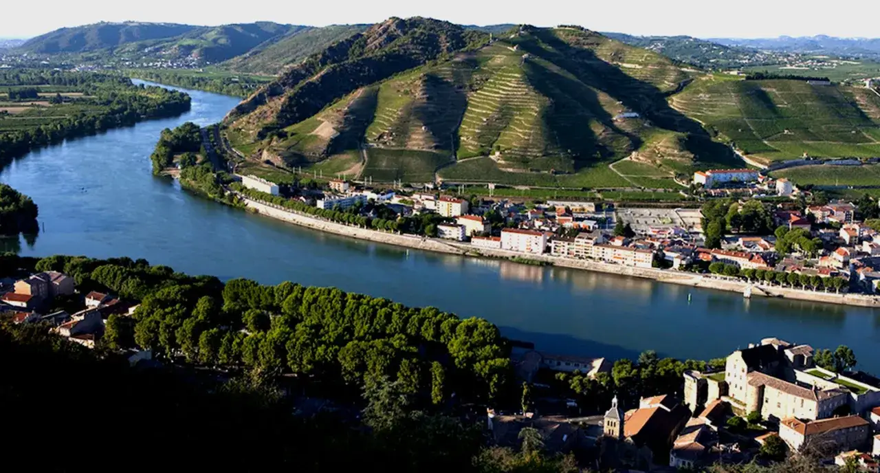Paesaggio del Rodano in Francia, con il fiume che serpeggia tra colline coltivate a vigneti e un villaggio pittoresco.