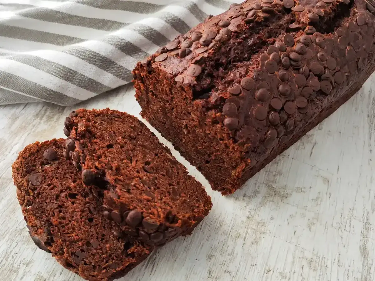 Saftiges bananenbrot mit schokolade, bestreut mit vielen schokostückchen. Zwei Scheiben liegen daneben.