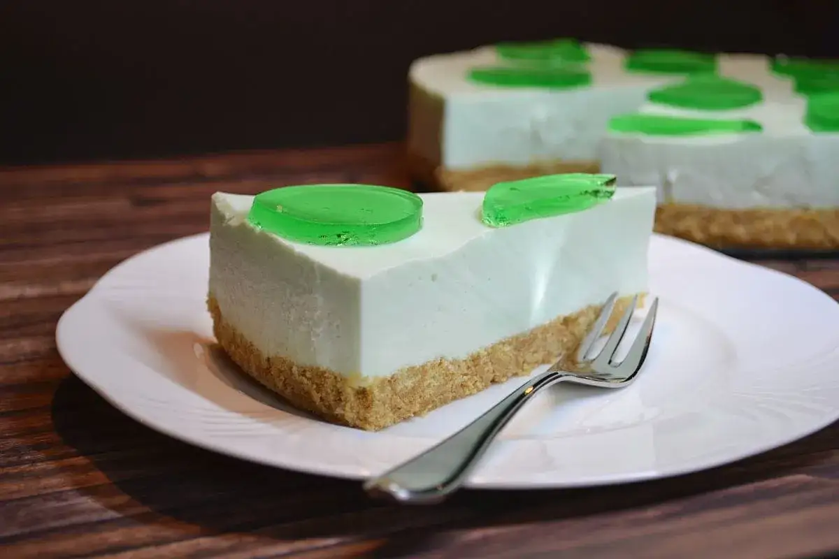 Ein Stück Philadelphia Torte Waldmeister mit grünem Gelee auf einem weißen Teller, daneben eine Gabel.