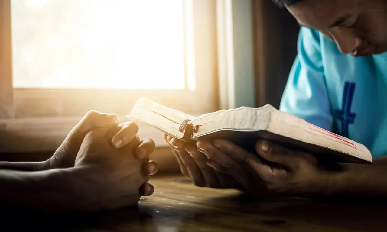A person reads a Bible and prays, embodying the spirit that god helps those who help themselves.