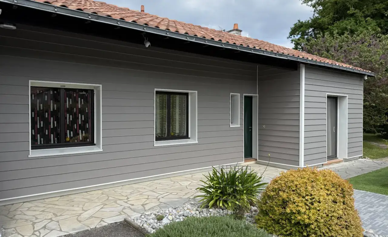 Maison moderne avec bardage gris, fenêtres et porte verte. Le revêtement extérieur assure une isolation par l'extérieur efficace.