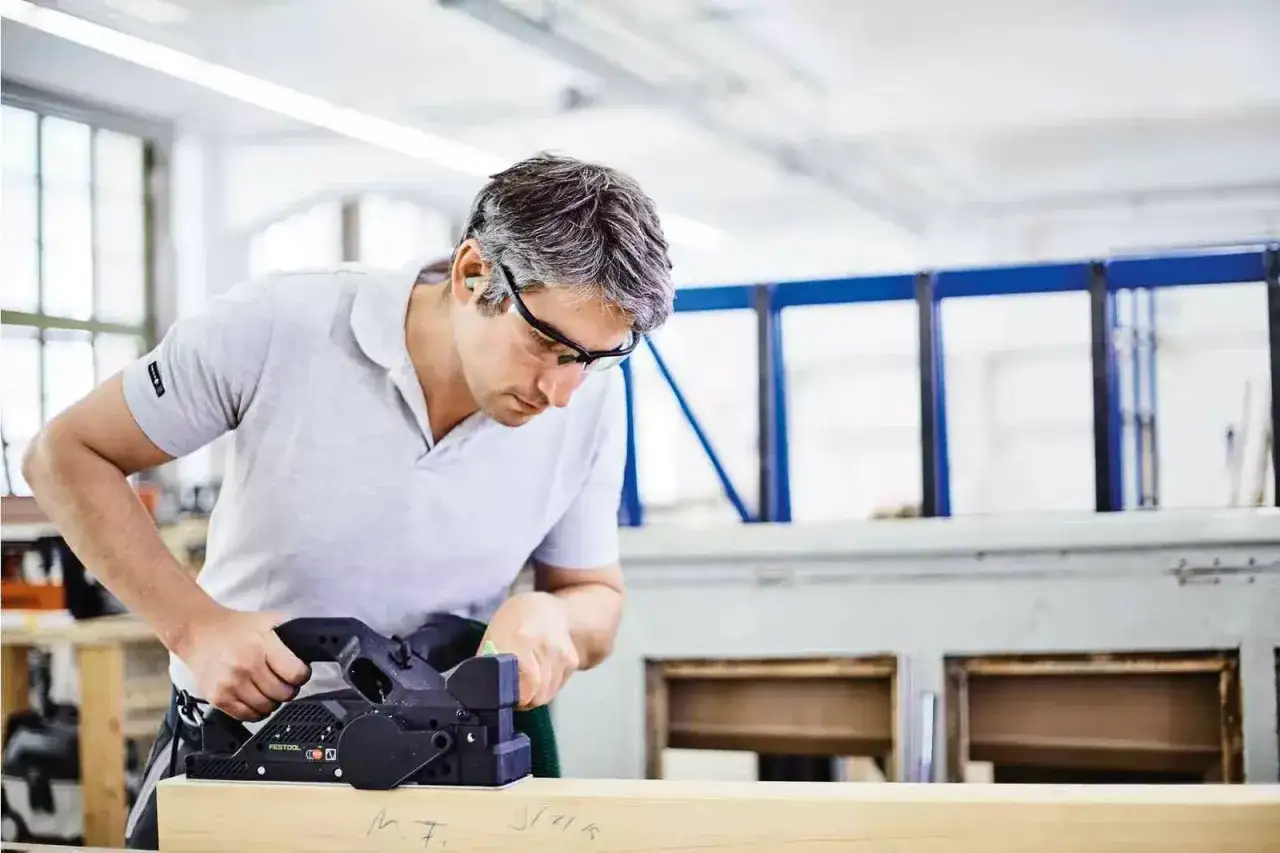 Artisan concentré utilisant le rabot Festool HL 850 pour lisser une pièce de bois dans un atelier.