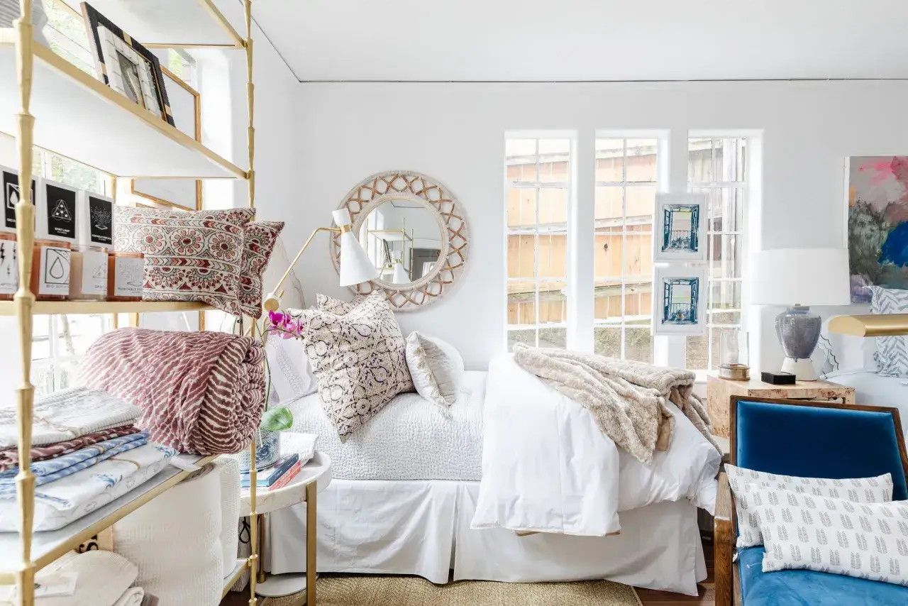 A cozy bedroom with a white bed, patterned pillows, and a plush throw. The bed features a white bed skirt, a classic example of sham bedding, adding a tailored look.