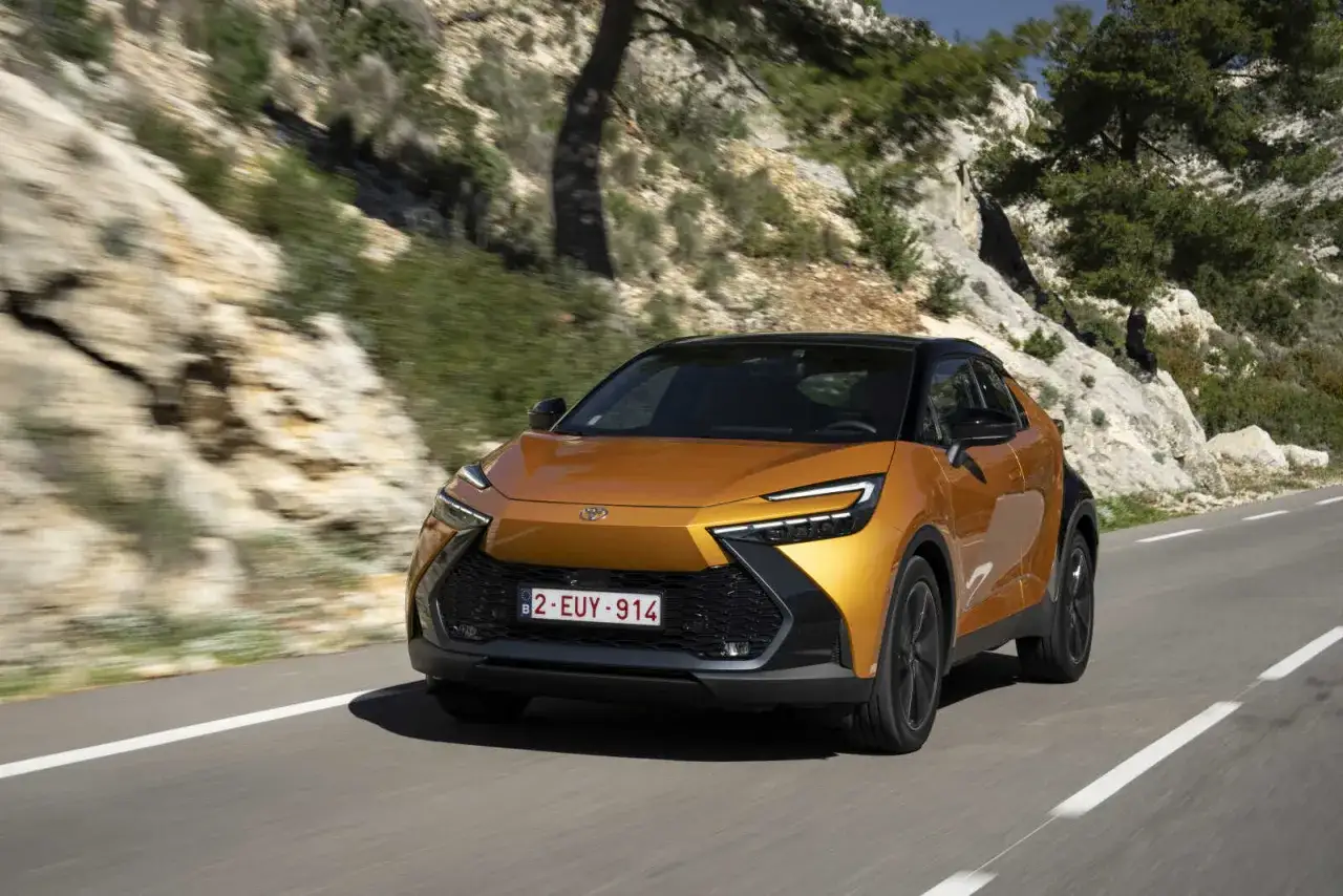 En orange Toyota C-HR Hybrid testas på en slingrande väg i bergig terräng.