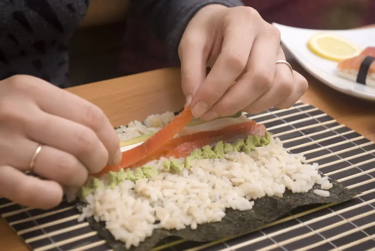 Händer lägger lax på ris och wasabi för att rulla sushi maki.