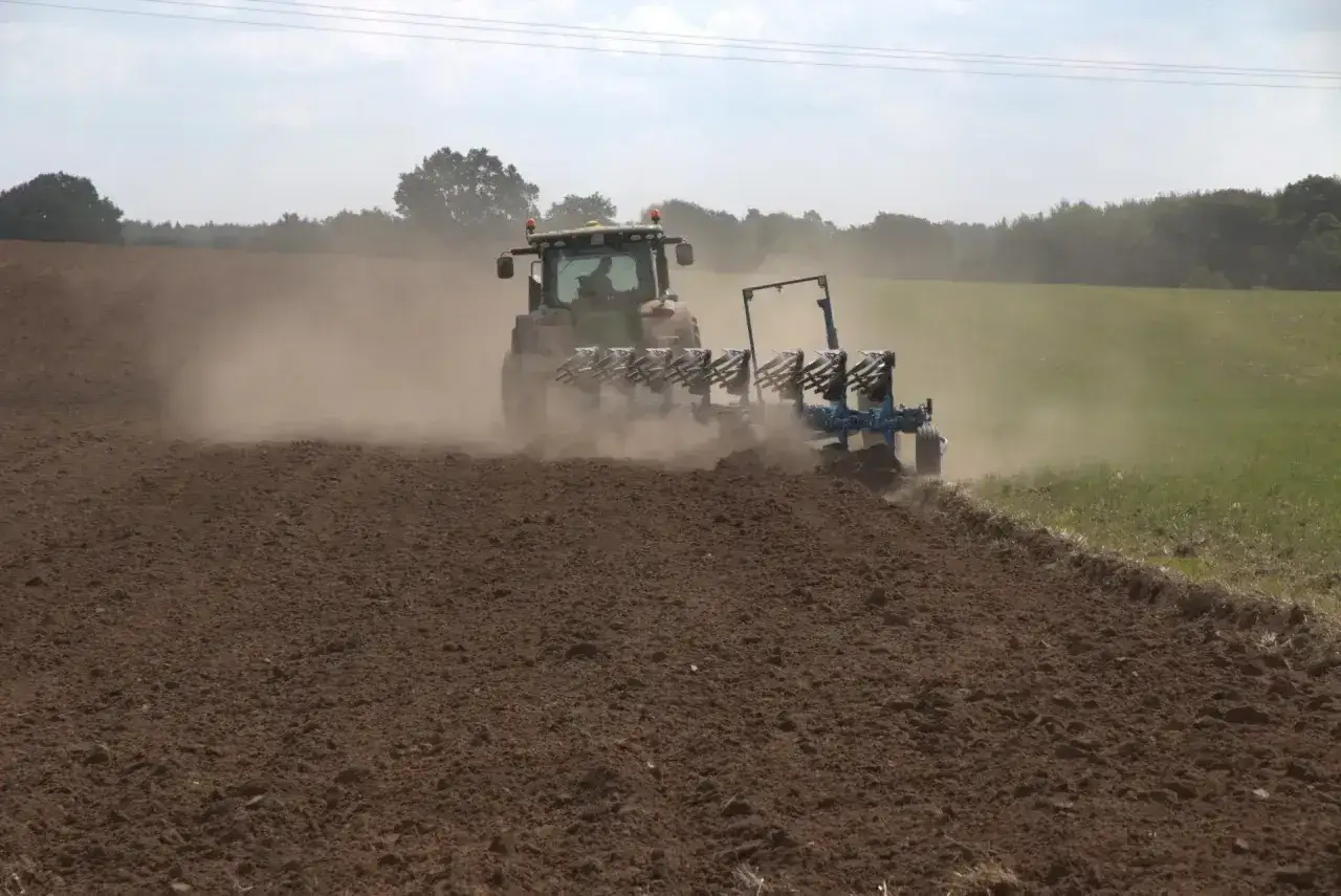 Traktor z pługiem orze pole, wzbijając tumany kurzu. To ważny etap przygotowania gleby, który może pomóc w jej odkwaszaniu.