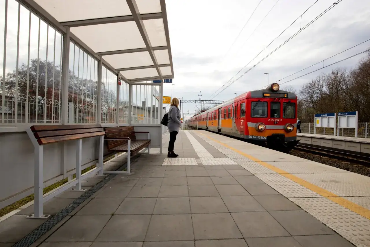 Kobieta czeka na pociąg PKP w Sołcu-Zdroju. Czerwono-pomarańczowy skład stoi na torach.