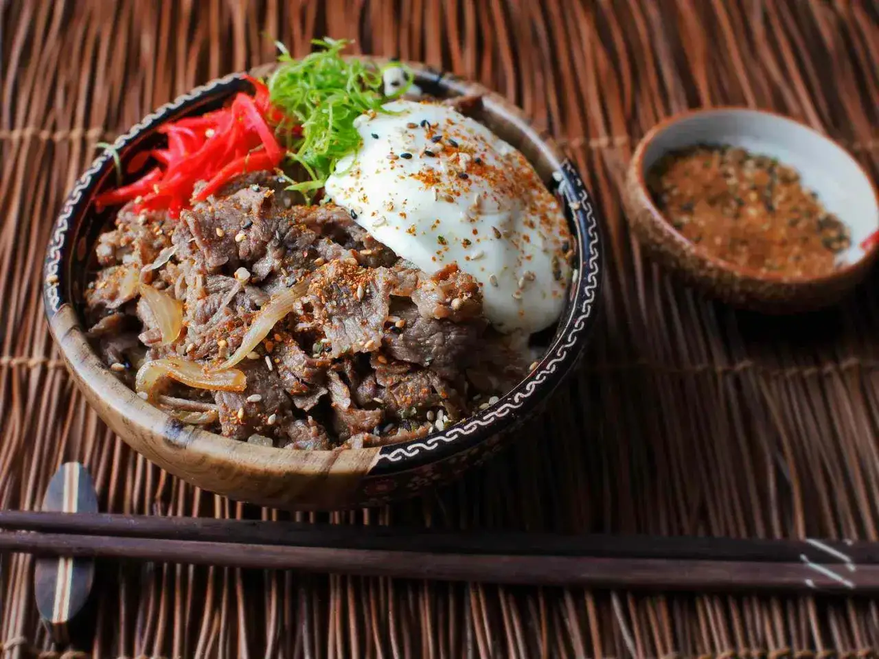 A delicious gyudon recipe bowl with tender beef, onions, a fried egg, pickled ginger, and green onions.