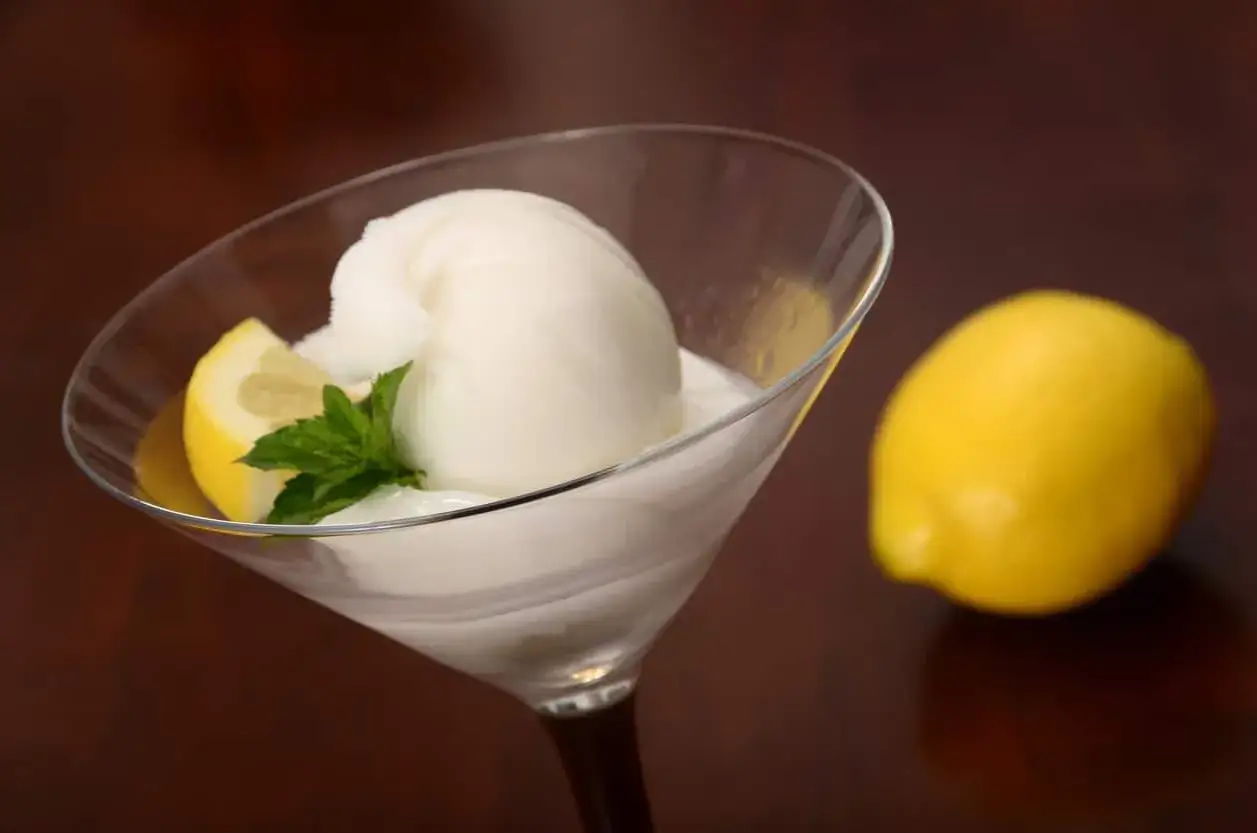 Glace colonel rafraîchissante dans un verre, garnie d'une tranche de citron et de menthe. Un citron entier repose à côté.