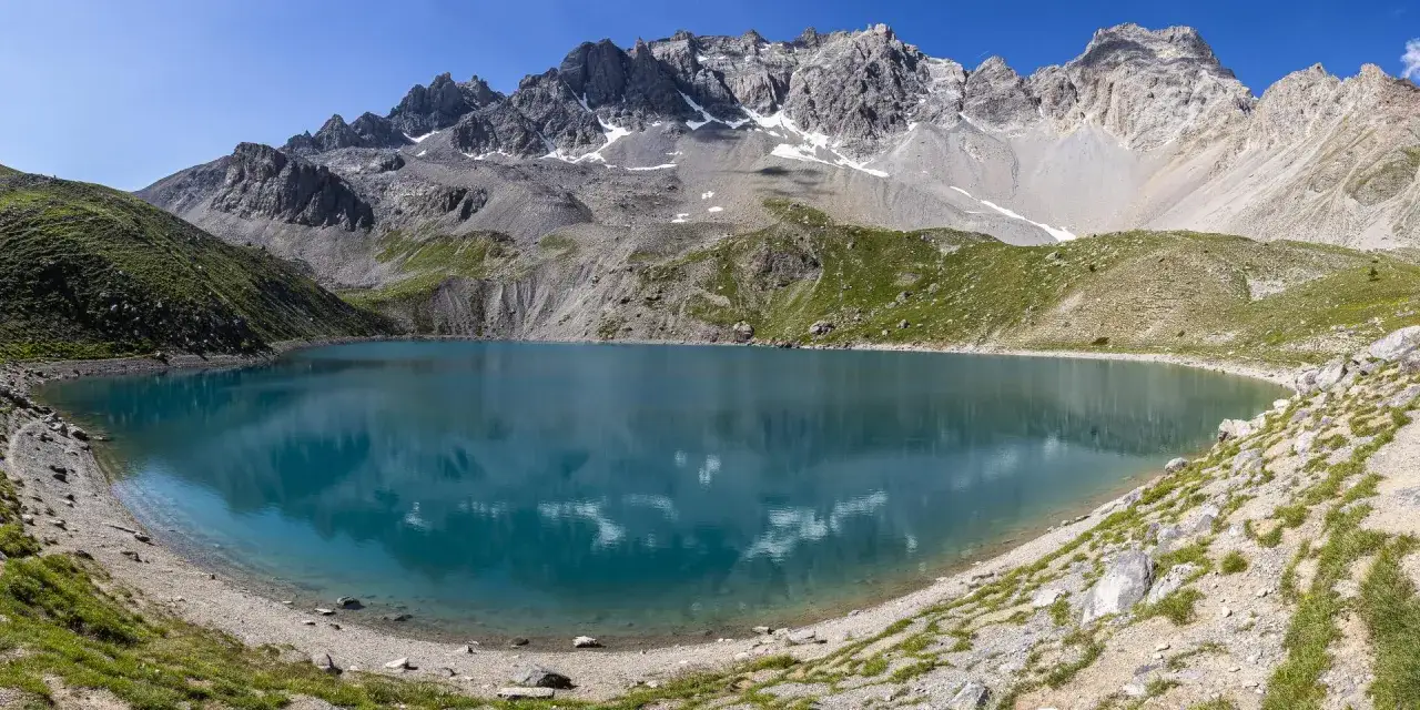 Magnifique lac Saint-Anne aux eaux turquoise, bordé de montagnes rocheuses et de pentes verdoyantes sous un ciel bleu éclatant.