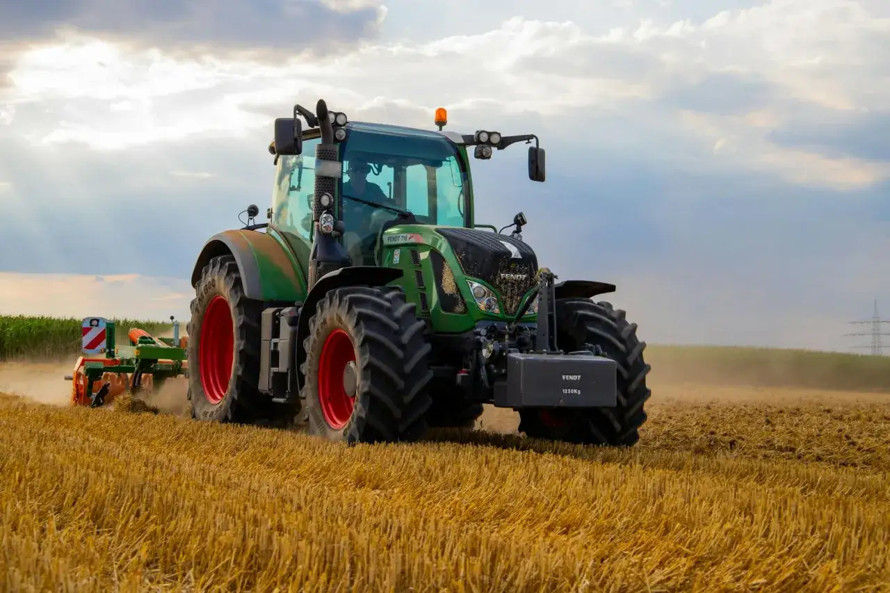 Zielony traktor Fendt 718 orze pole, wzbijając kurz. To potężna maszyna, która pomaga w pracy na roli.