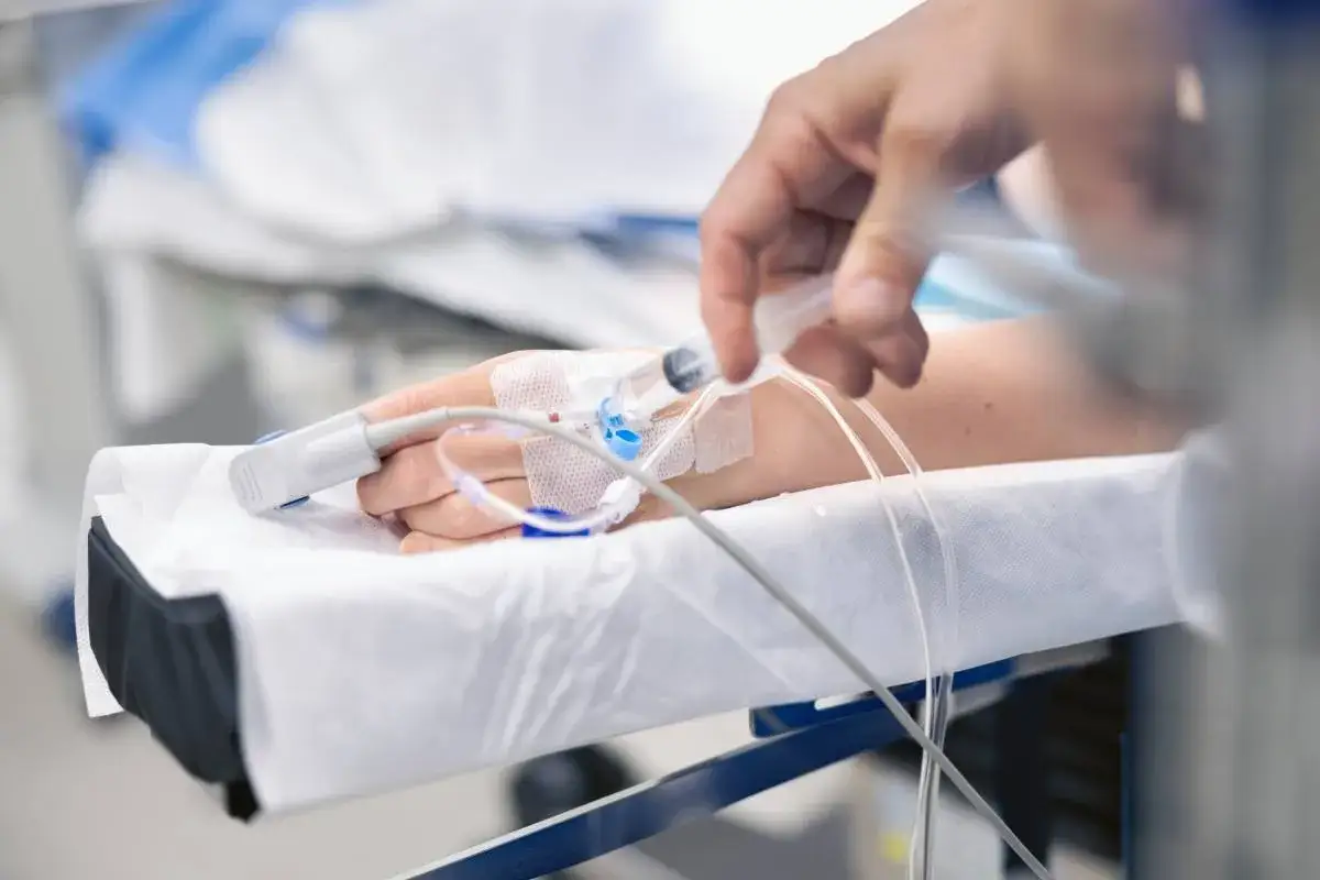 Dłoń pacjenta z pulsoksymetrem i wenflonem, do którego podawany jest propofol.