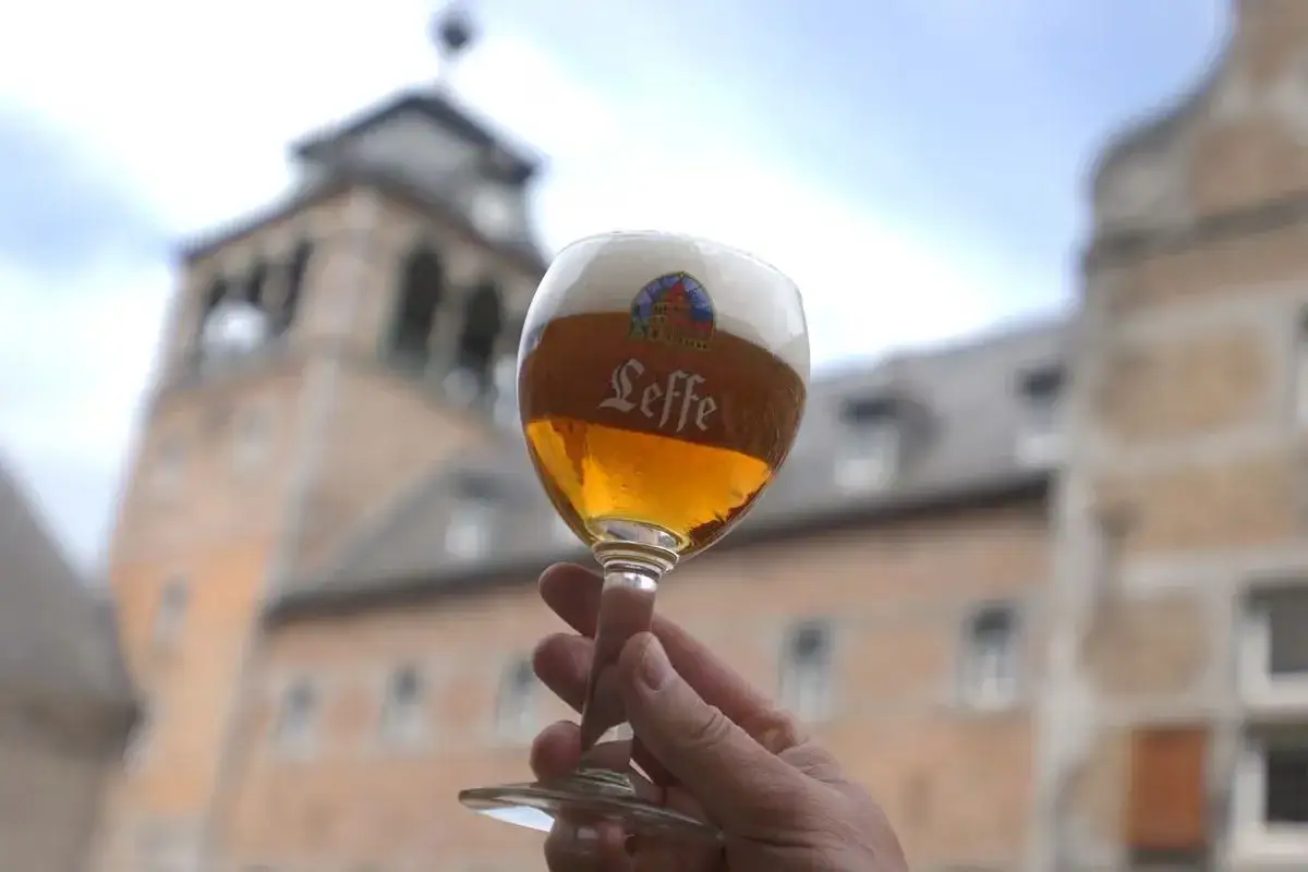 Verre de bi&egrave;re Leffe, avec le logo bien visible, devant un b&acirc;timent historique.