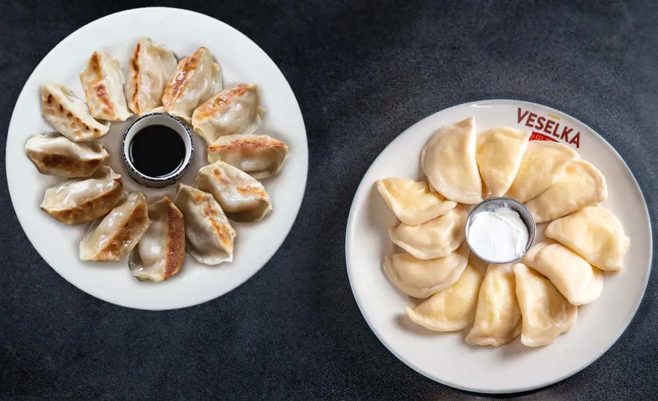Dwa talerze z pierogami: po lewej smażone pierogi gyoza z sosem sojowym, po prawej gotowane pierogi z Veselka ze śmietaną.