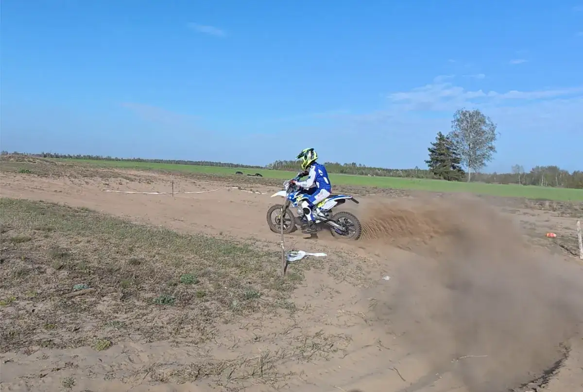 Motocyklista w kasku i stroju crossowym pokonuje zakręt na piaszczystym torze, wzbijając tumany kurzu. Od ilu lat można jeździć crossem? Odpowiedź zależy od umiejętności i treningu!