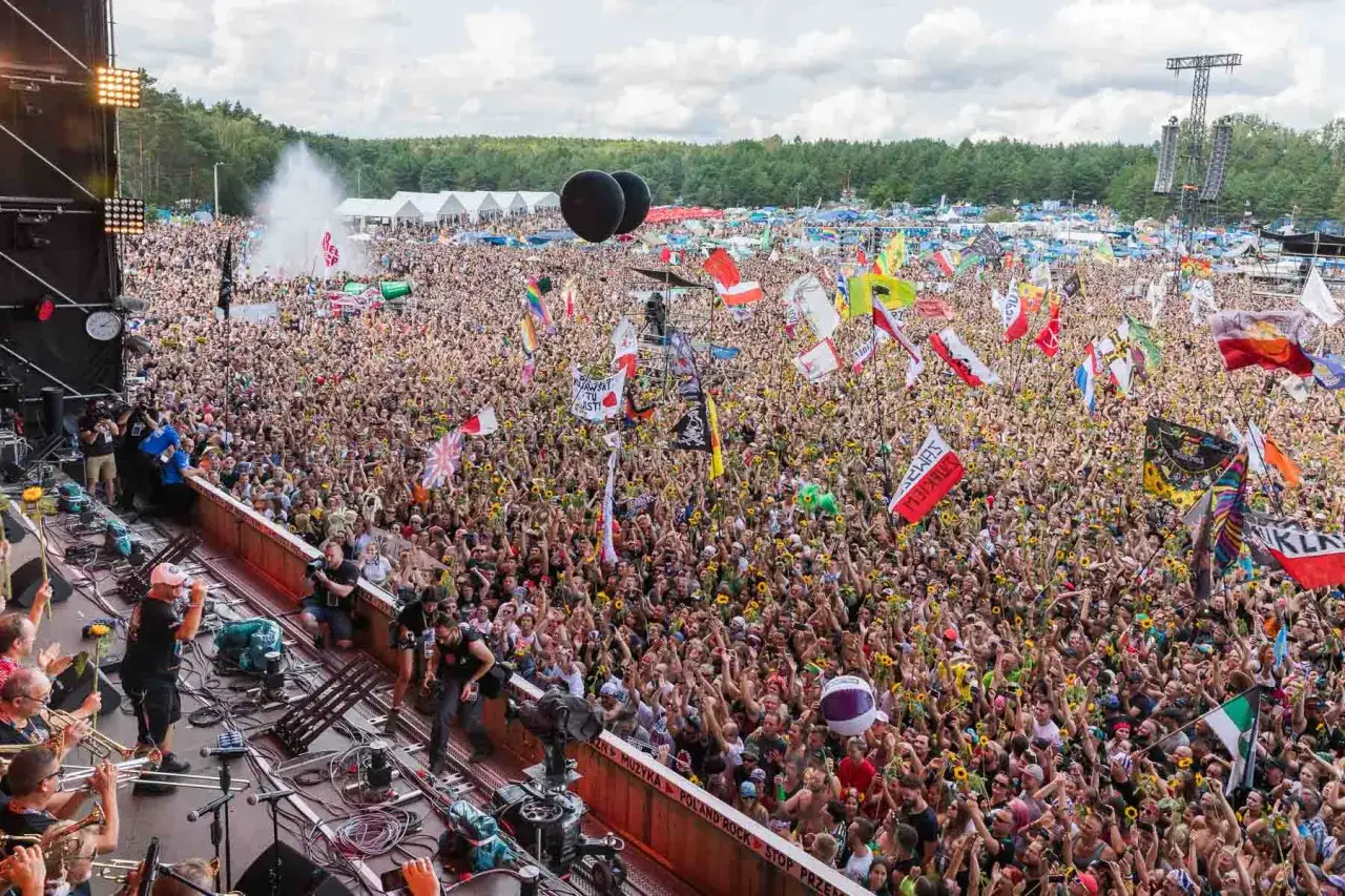 Ogromny tłum na festiwalu, ludzie machają flagami i kwiatami. To właśnie jest tournee, czyli koncertowa podróż zespołu.