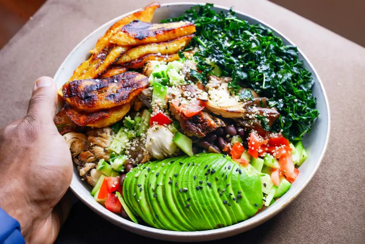 Una ciotola colorata con avocado, platano fritto, verdure e quinoa. Ottimi quinoa valori nutrizionali per un pasto completo.