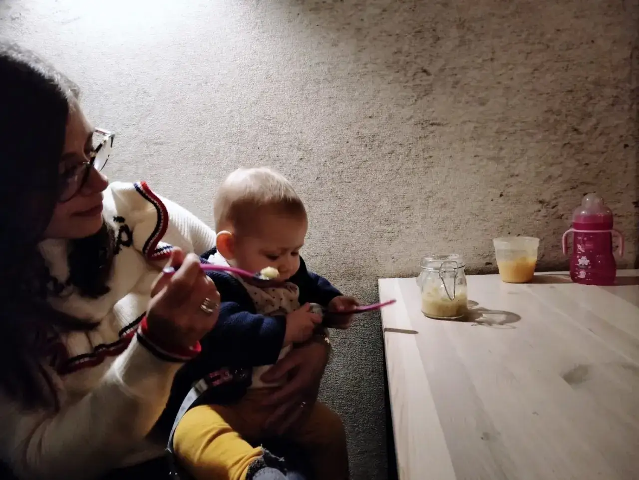 Mamma dà la pappa al suo bimbo fuori casa, con un vasetto di omogeneizzato e biberon pronti.