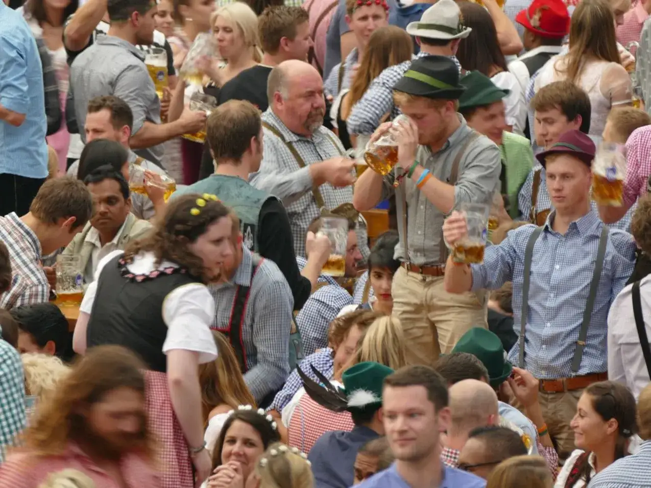 Menschen in Tracht feiern und trinken Bier. Sie fragen sich, wie lang geht die Wiesn?