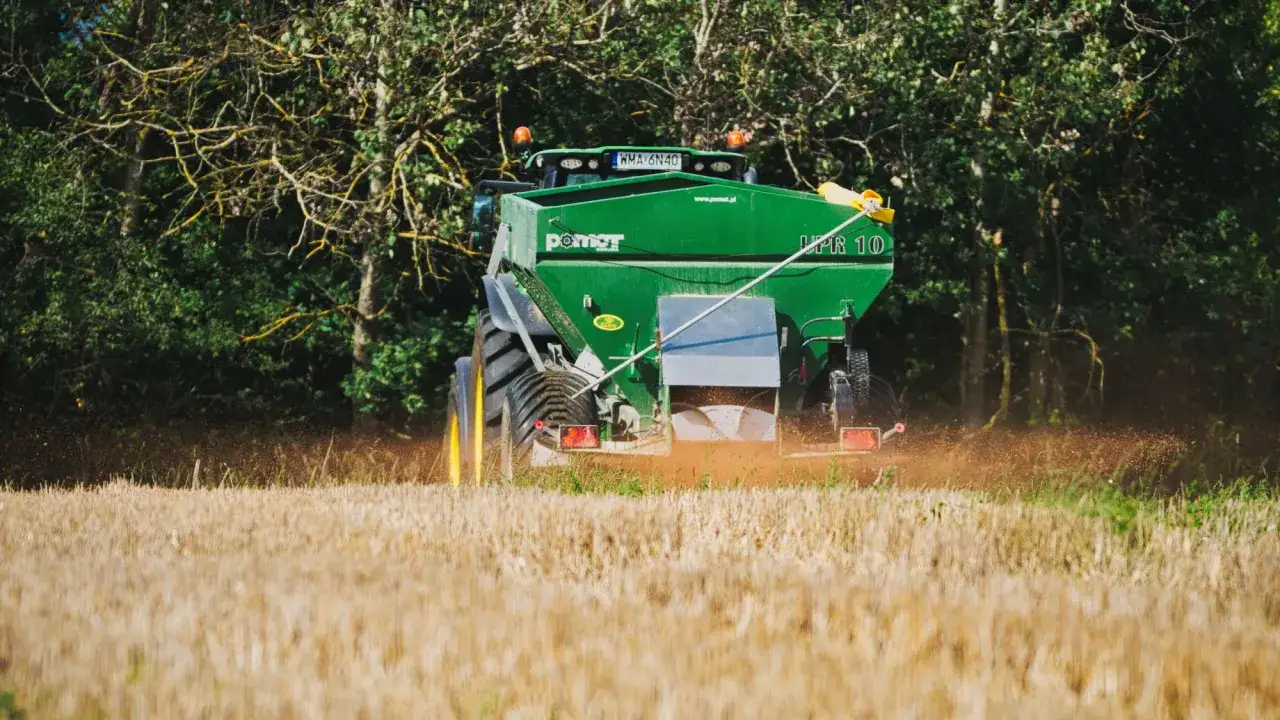 Zielony traktor rozsiewa wapno magnezowe na polu.