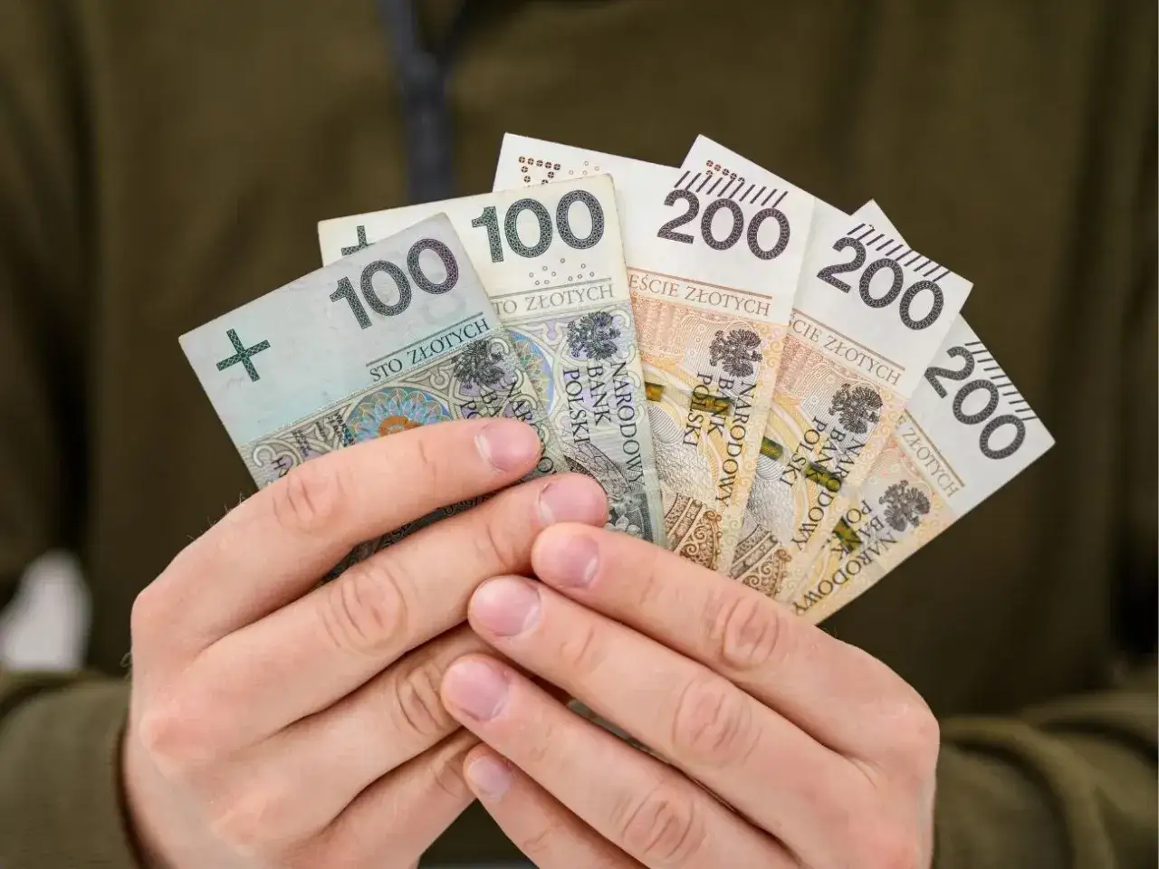 Dłonie trzymające banknoty 100 i 200 złotych. Taka kwota to już coś, można pomyśleć o wakacjach, albo o spłaceniu raty 